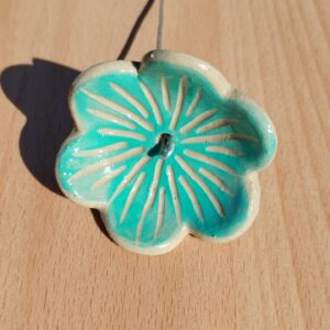 fleur en céramique montée sur tige. Fond couleur turquoise, avec nervures gravées