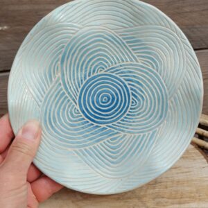 Assiette décorative ondulée en céramique. Poterie colorée en dégradé de bleu avec motif de lignes gravées Assiette décorative ondulée en céramique. Poterie colorée en dégradé de bleu avec motif de lignes gravées évoquant les mouvements de l'eau