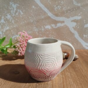 Tasse en céramique artisanale. Fond en dégradé de rose. Motif de fleurs gravé