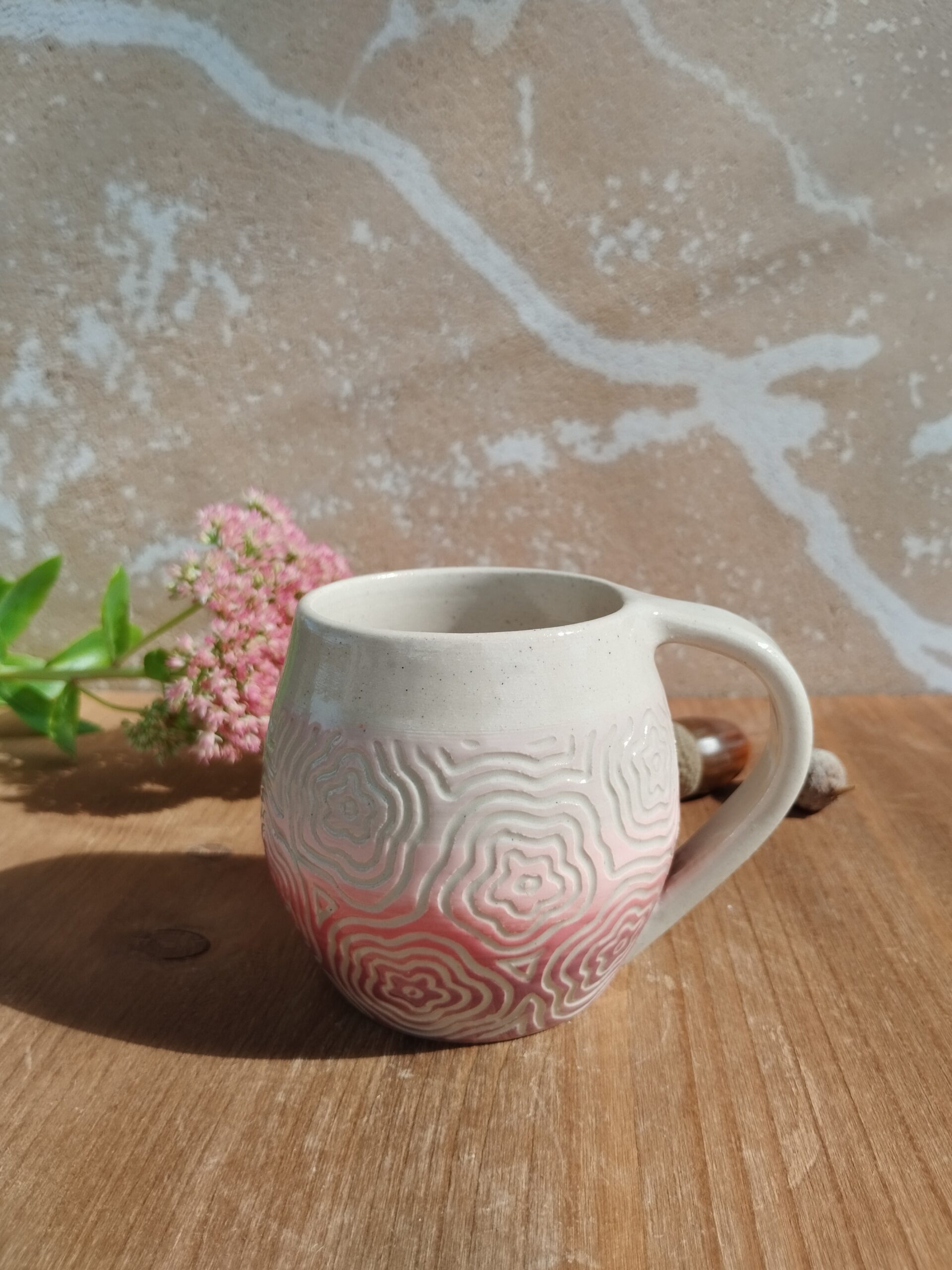 Tasse en céramique artisanale. Fond en dégradé de rose. Motif de fleurs gravé