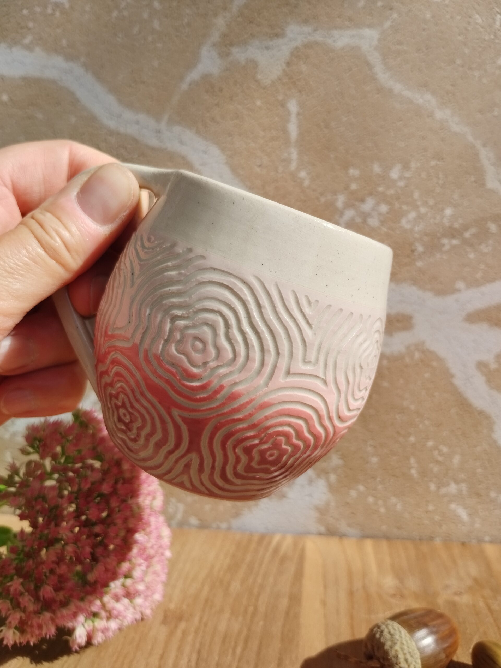 Tasse en céramique artisanale. Fond en dégradé de rose. Motif de fleurs gravé