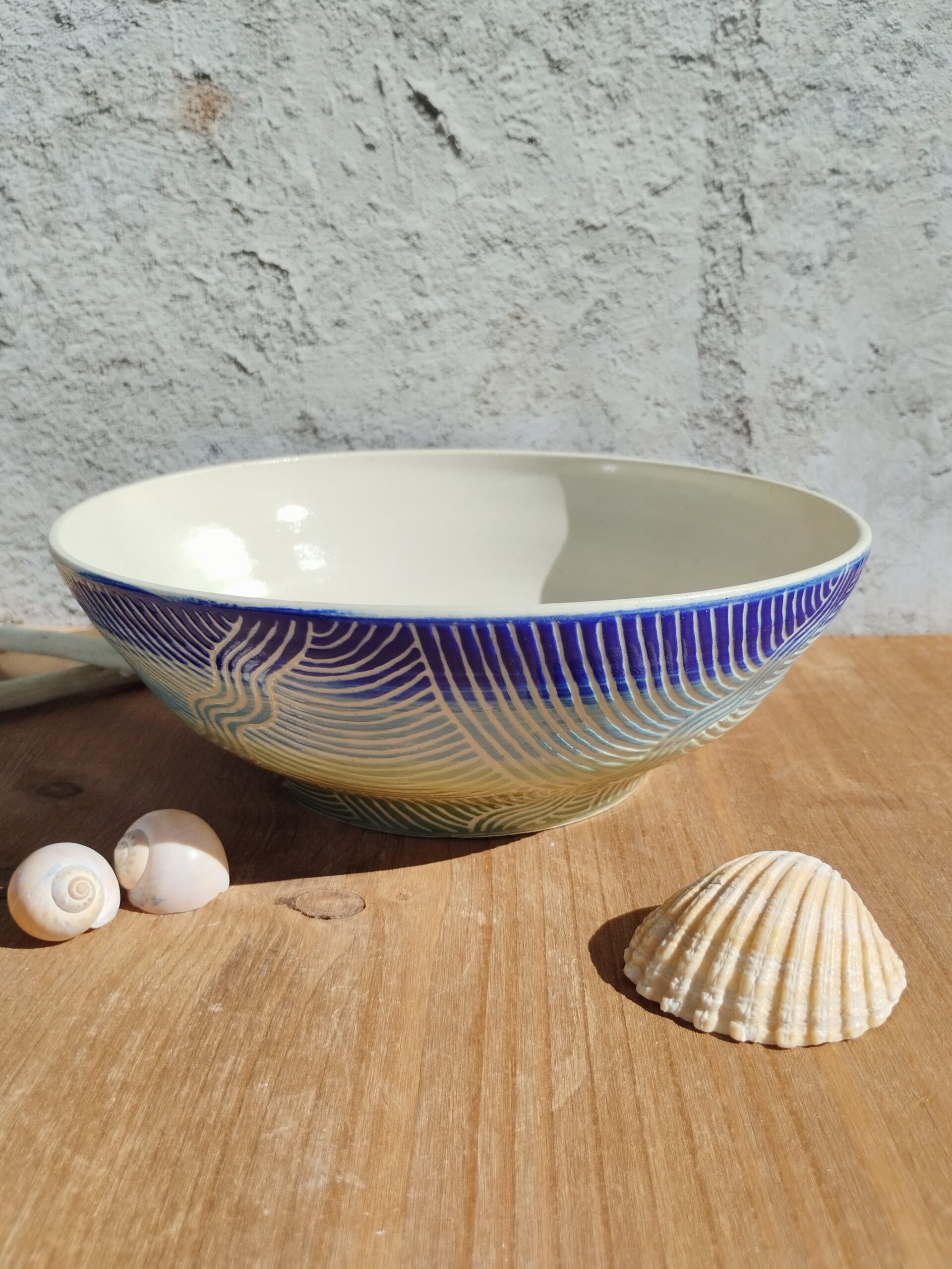 saladier en céramique artisanale. Fond en dégradé de bleu et vert. Motif de lignes gravées rappelant les mouvements de l'eau