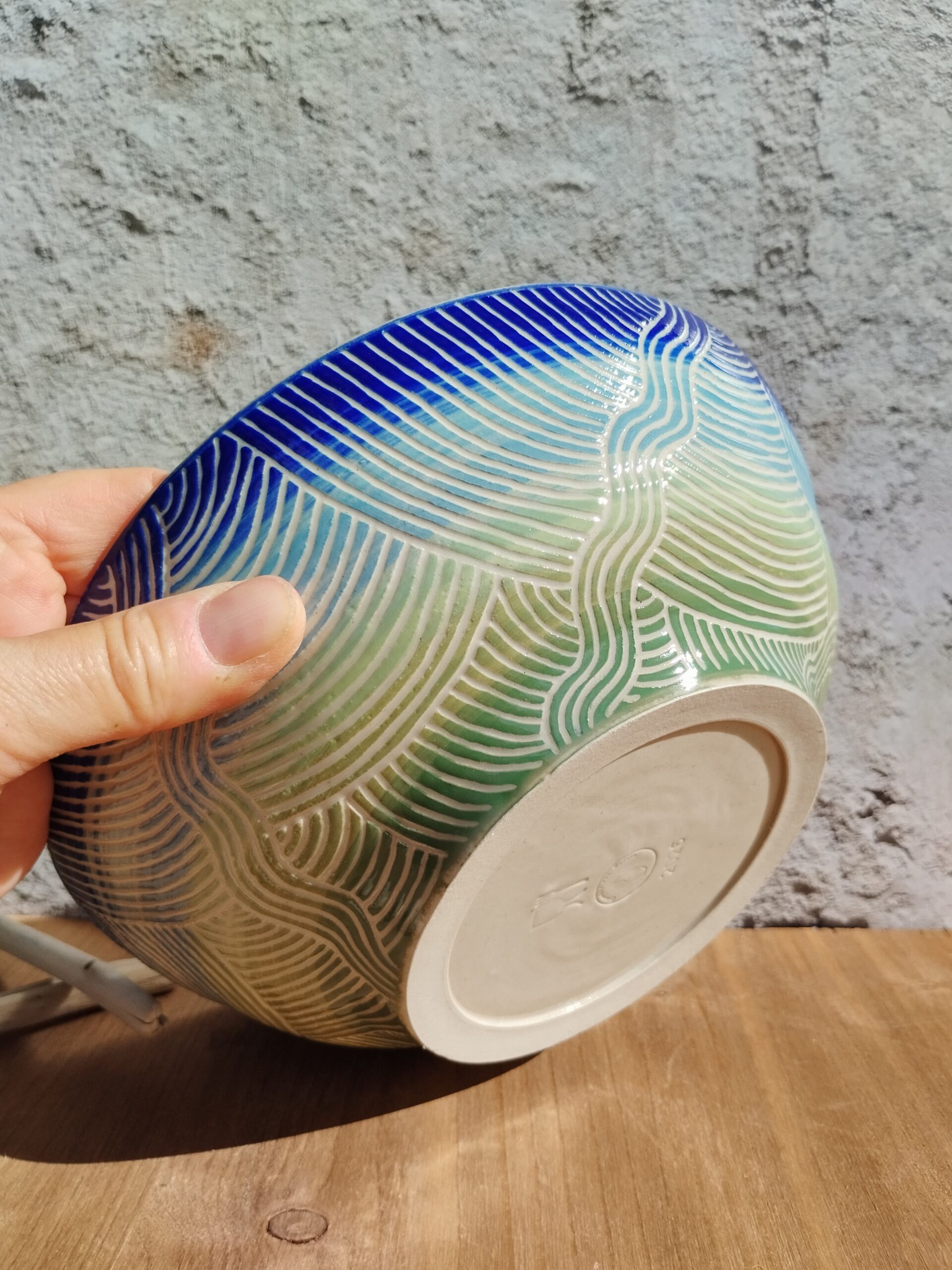 saladier en céramique artisanale. Fond en dégradé de bleu et vert. Motif de lignes gravées rappelant les mouvements de l'eau