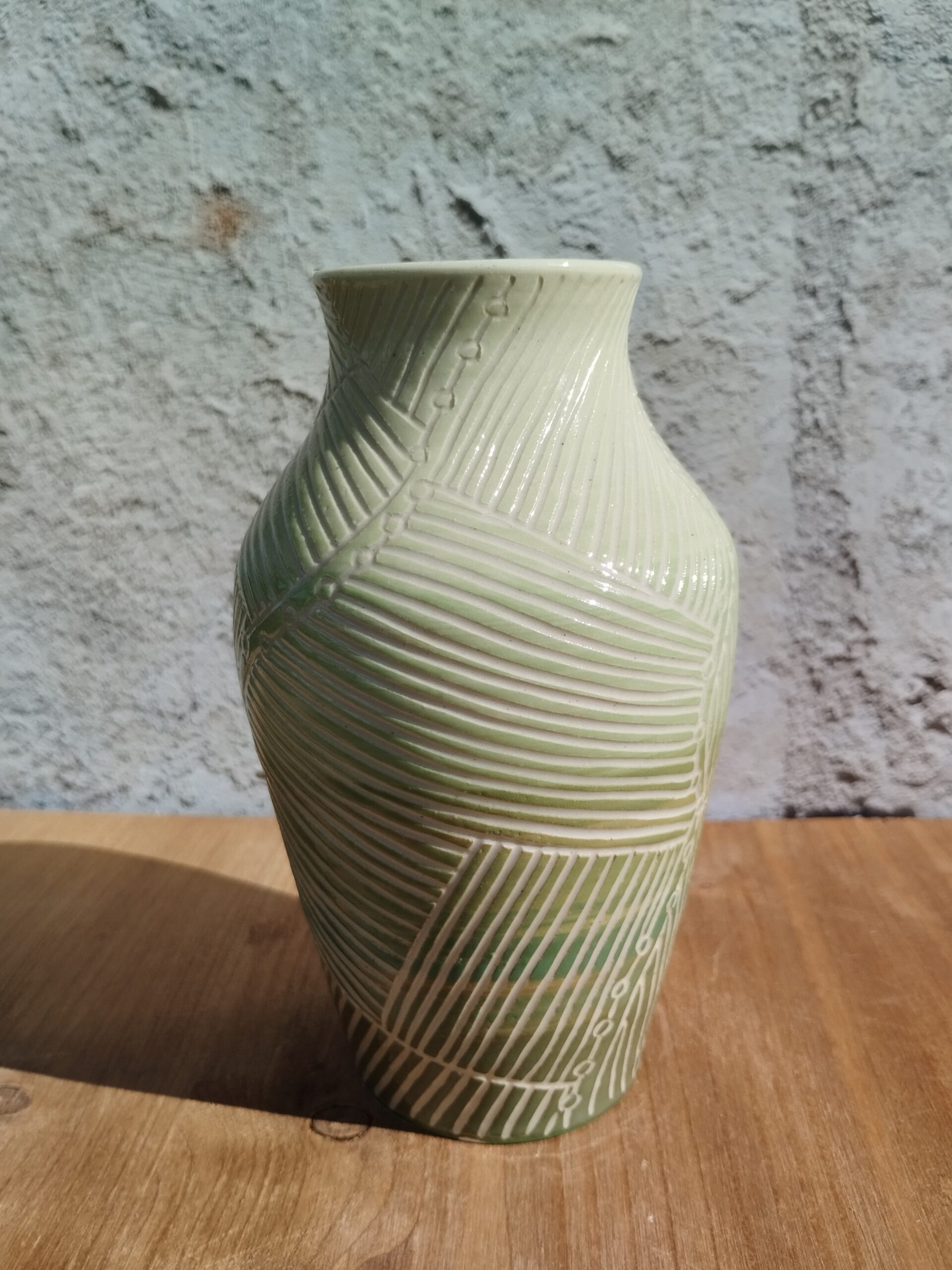 Vase en céramique artisanale. Fond coloré en dégradé de vert. Motif de lignes gravées