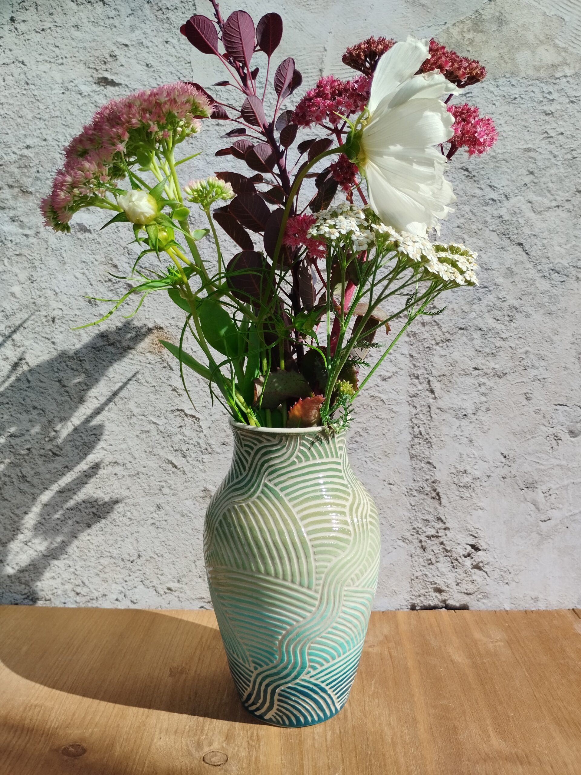 vase en céramique artisanale. Fond en dégradé de vert et bleu. Motif de lignes gravées