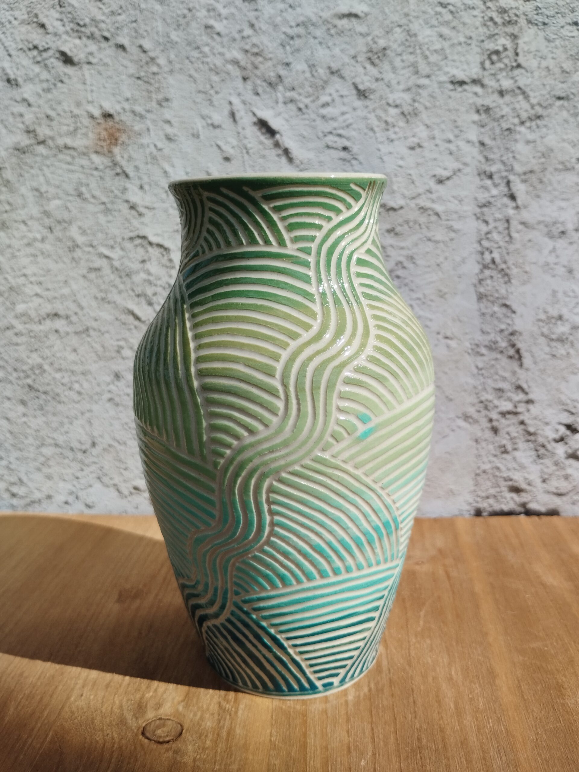 vase en céramique artisanale. Fond en dégradé de vert et bleu. Motif de lignes gravées