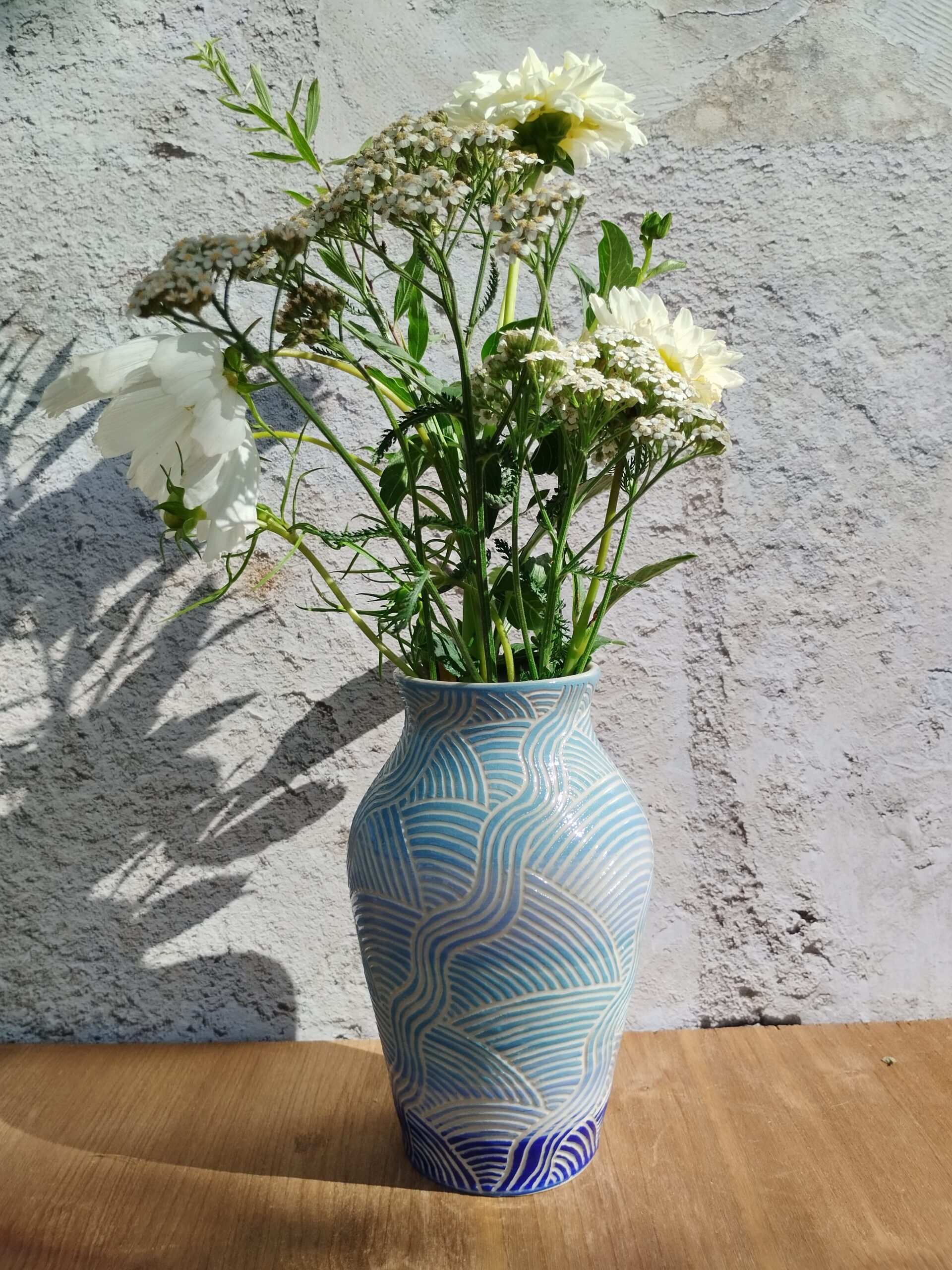 vase en céramique artisanale. Fond en dégradé de bleu. Motif de lignes gravées