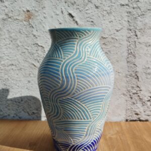 vase en céramique artisanale. Fond en dégradé de bleu. Motif de lignes gravées