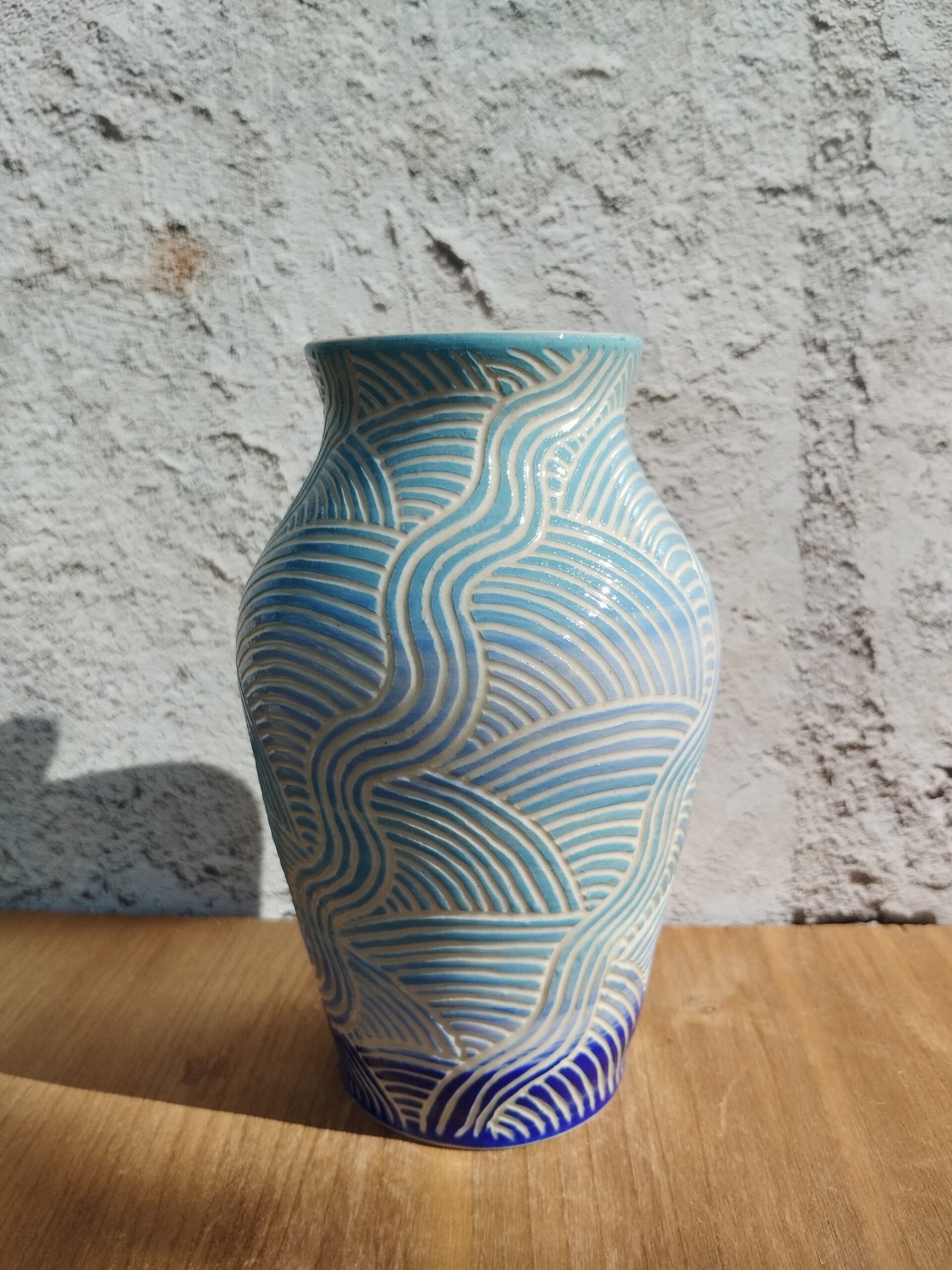 vase en céramique artisanale. Fond en dégradé de bleu. Motif de lignes gravées