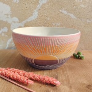 Saladier en céramique artisanale. Fond en dégradé rose orange bleu. Motif gravé soleil couchant sur l'eau.